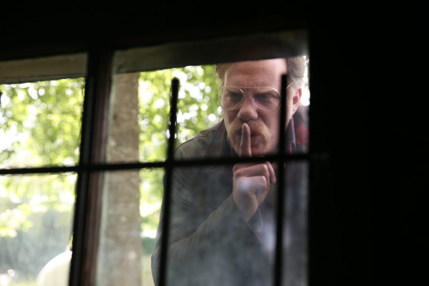 The antagonist gesturing for silence through a barred window in Alone
