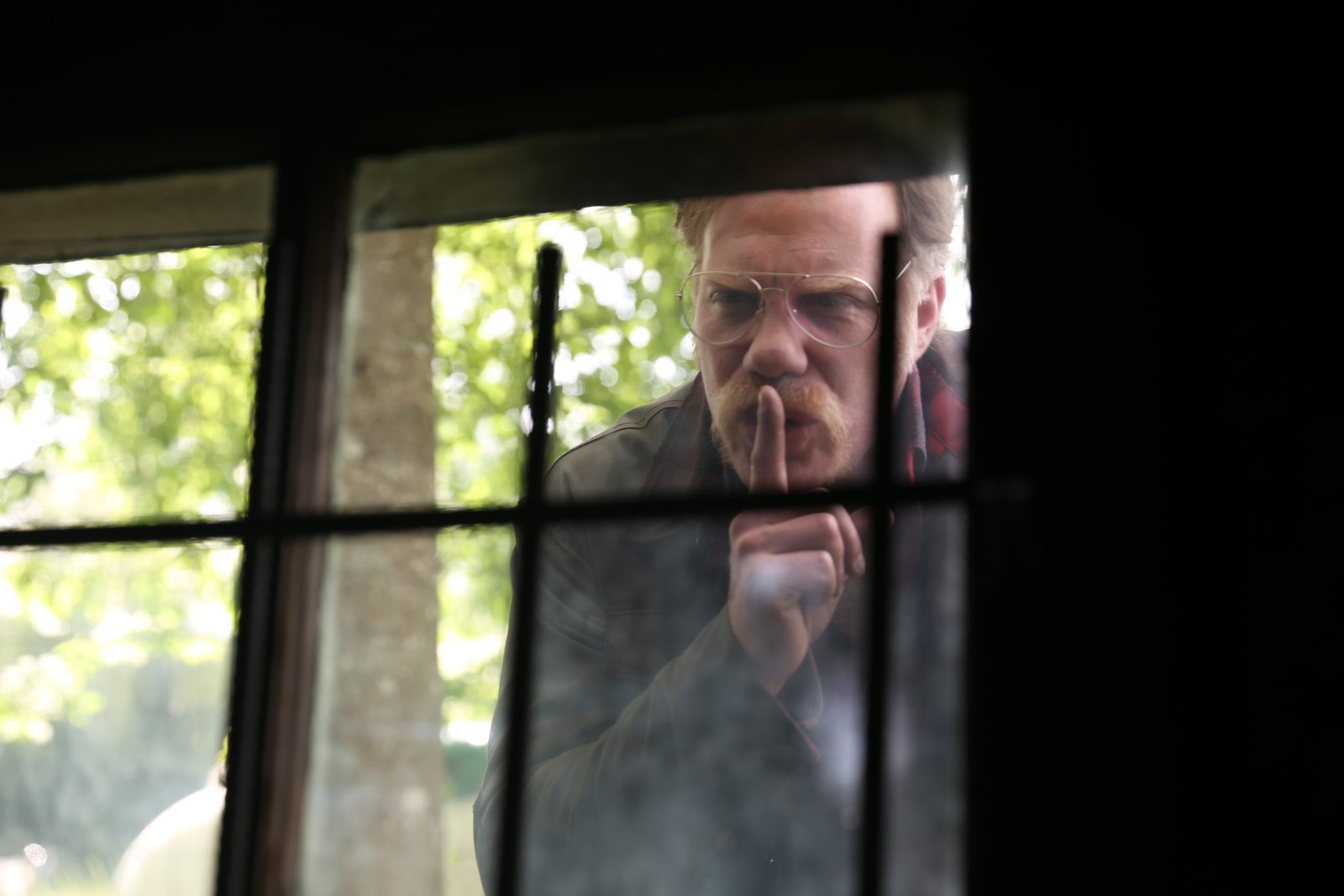 The antagonist gesturing for silence through a barred window in Alone
