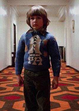 Danny Torrance standing alone in the symmetrical, patterned hallway of the Overlook Hotel in The Shining (1980)