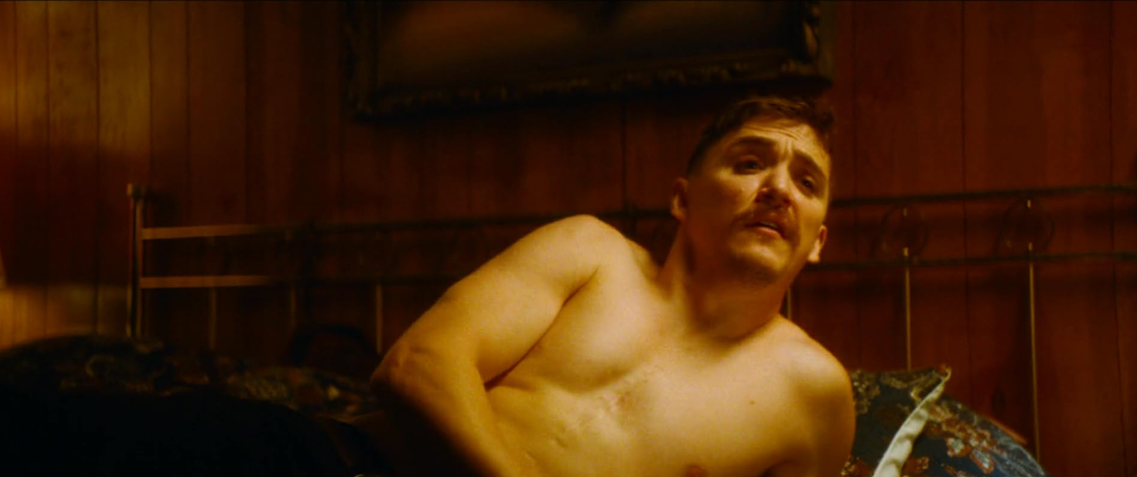 The Demon sitting up in a wood-panelled motel bedroom in Strange Darling