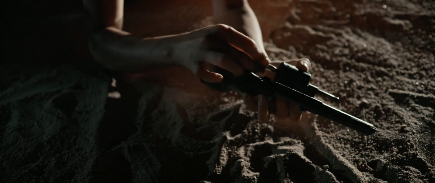 Close-up of hands loading a revolver in the dark desert sand at night