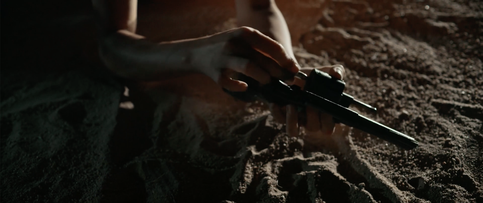 Close-up of hands loading a revolver in the dark desert sand at night