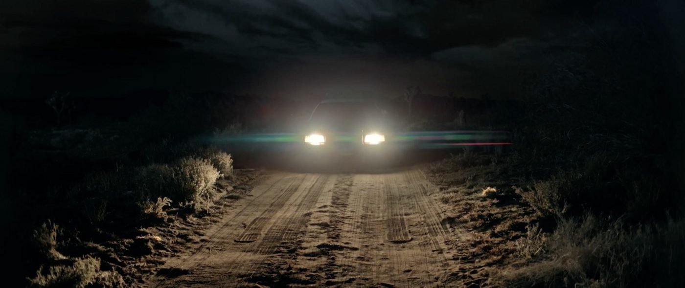 A car's headlights piercing the darkness on an empty desert road at night