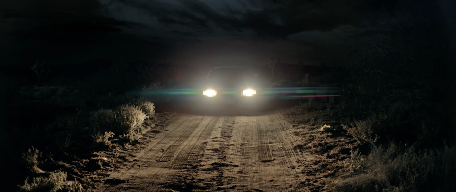 A car's headlights piercing the darkness on an empty desert road at night