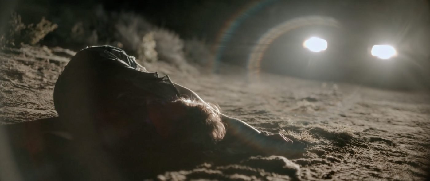 A body lying in the dark desert as a vehicle's headlights approach, Blood Star's opening ritual