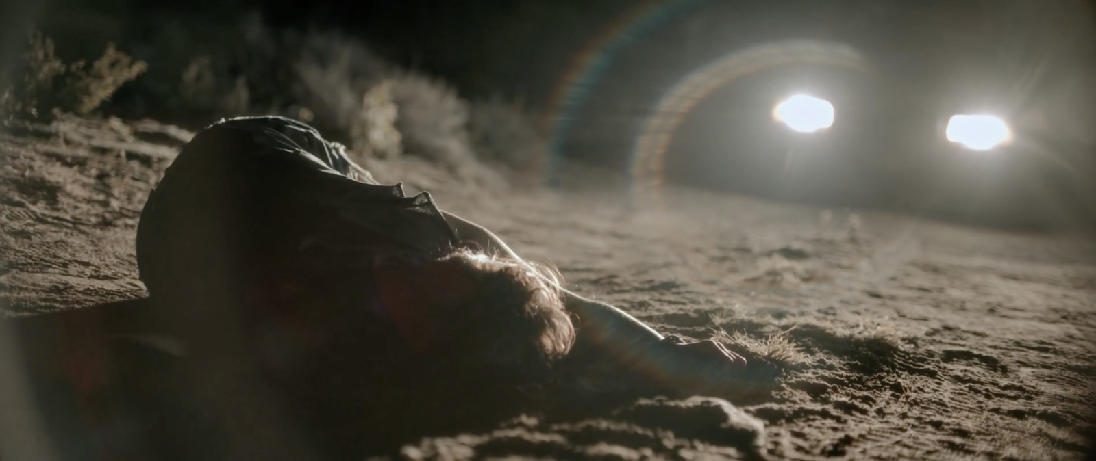 A body lying in the dark desert as a vehicle's headlights approach, Blood Star's opening ritual