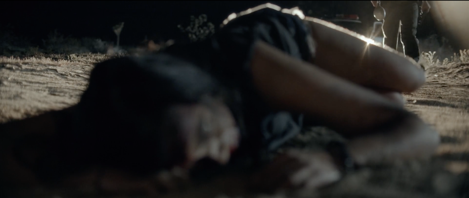 A bloodied woman lying in the dark desert as the sheriff approaches in the background