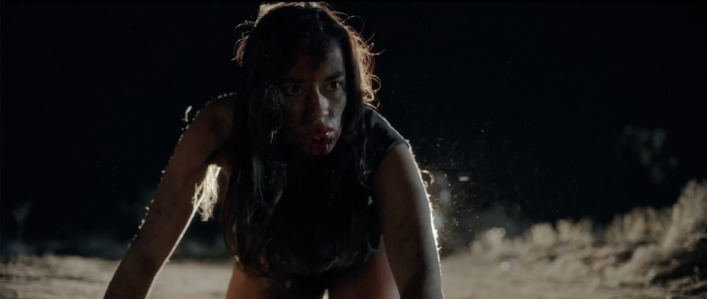 A bloodied woman crawling forward through the dark desert at night