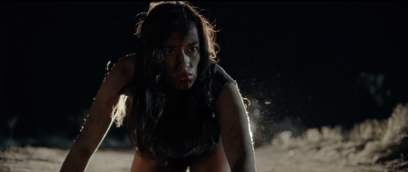 A bloodied woman crawling forward through the dark desert at night