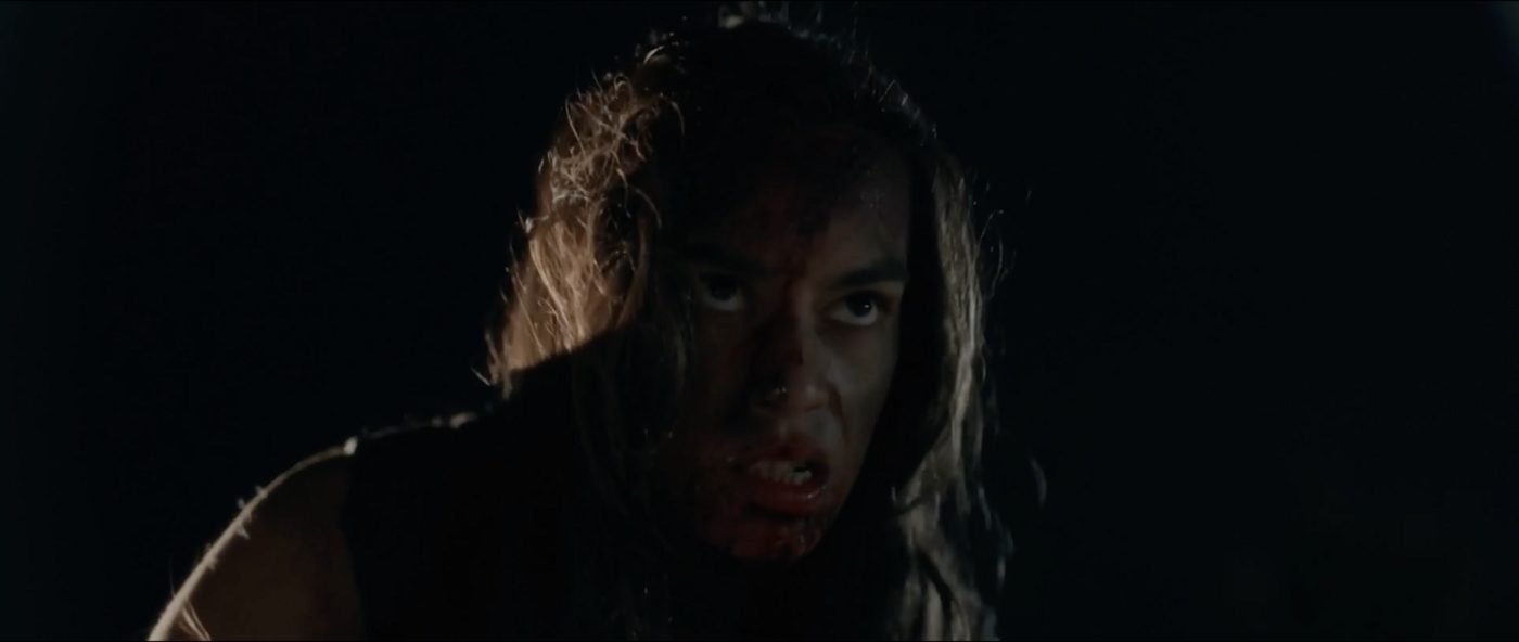 Extreme close-up of a woman's bloodied face in profile against total darkness