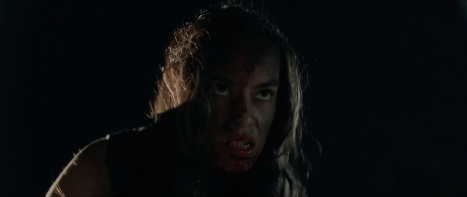 Extreme close-up of a woman's bloodied face in profile against total darkness