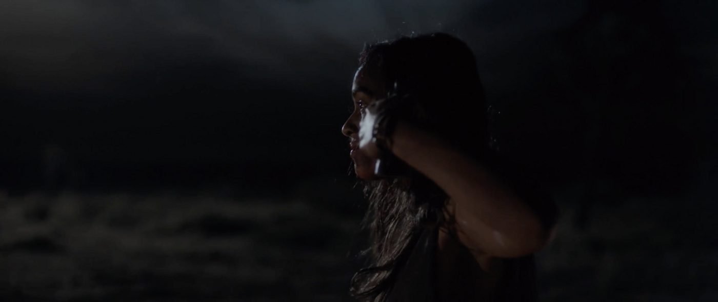 A woman walking toward a car's headlights on a dark desert road at night
