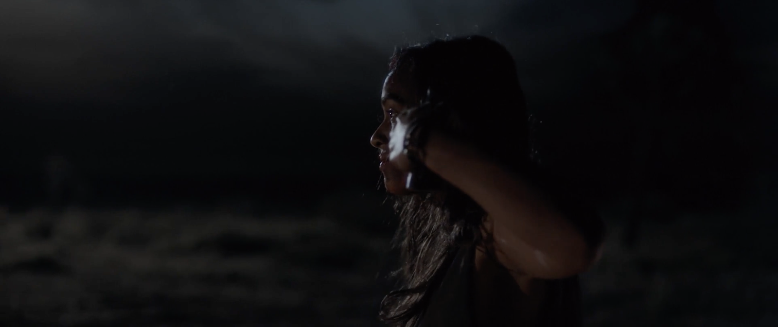 A woman walking toward a car's headlights on a dark desert road at night