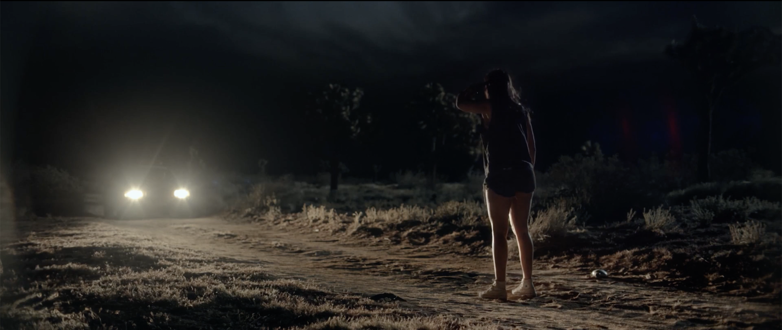 A car's headlights cutting through total darkness on an empty desert road at night