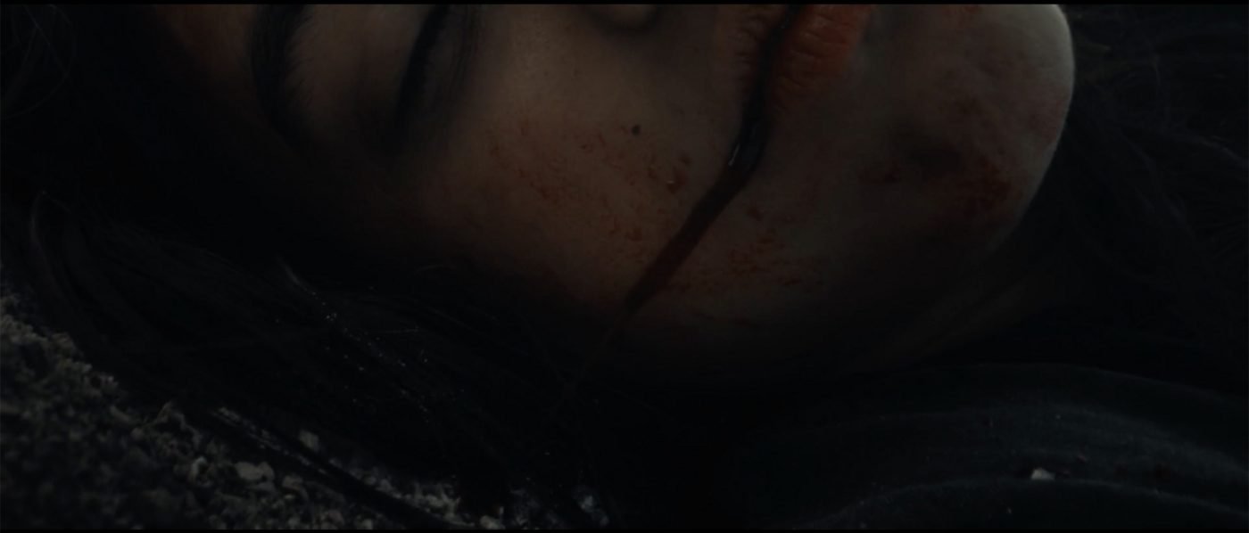 Extreme close-up of Bobbi's blood-streaked face, eyes closed, playing dead in Blood Star