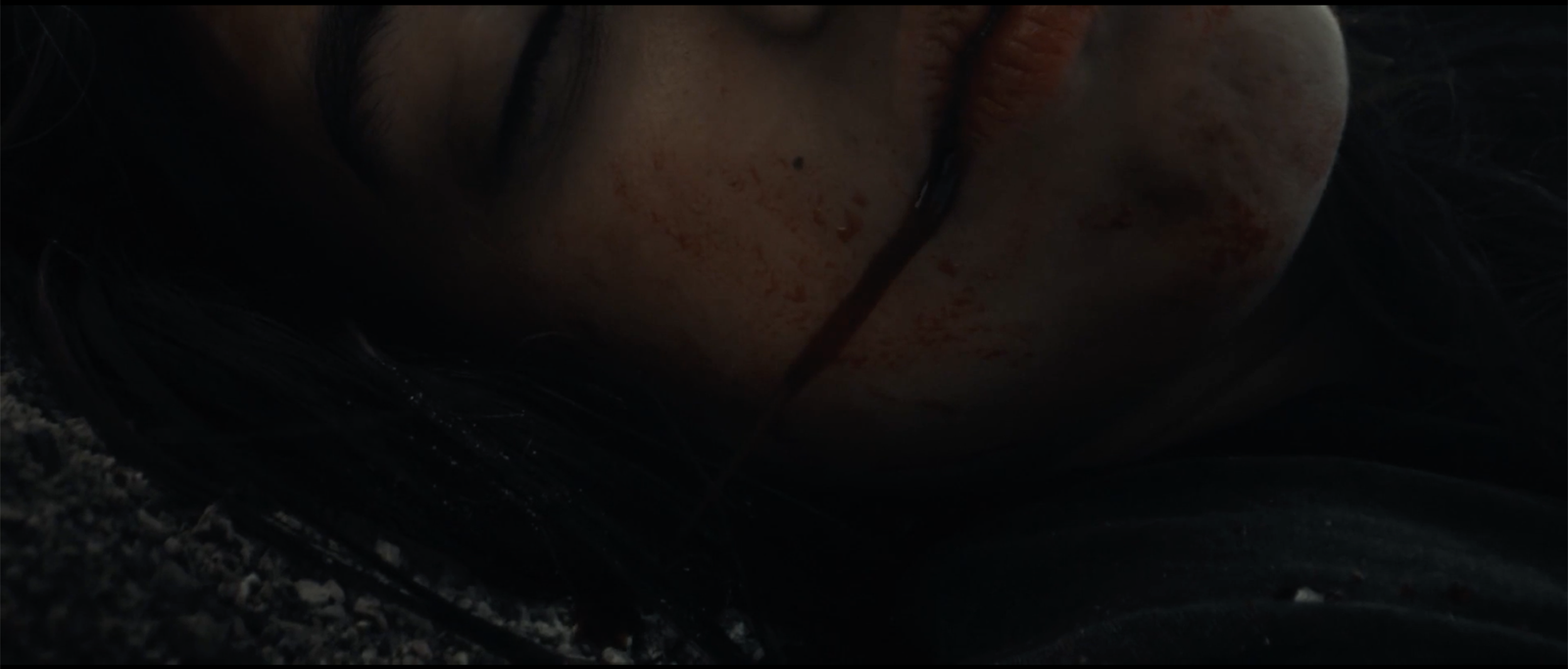 Extreme close-up of Bobbi's blood-streaked face, eyes closed, playing dead in Blood Star