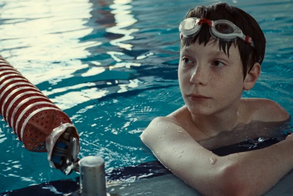 A boy in swimming goggles looking warily at a pool lane rope in The Plague (2025)