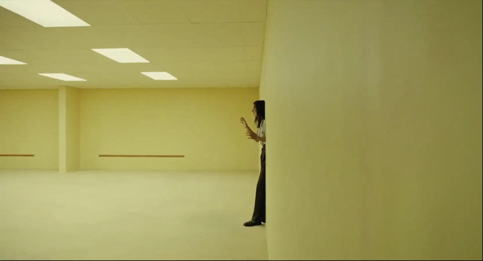 A woman searching an endless, featureless yellow wall in an empty Backrooms room