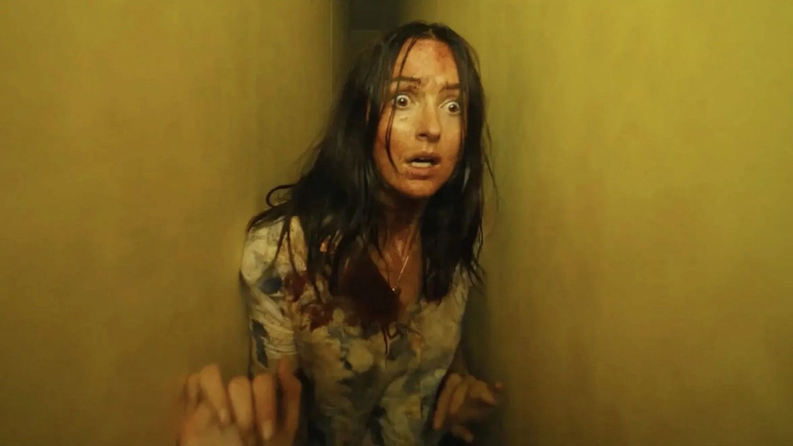 A bloodied woman pressed against a wall in an endless yellow fluorescent-lit corridor in Backrooms (2026)
