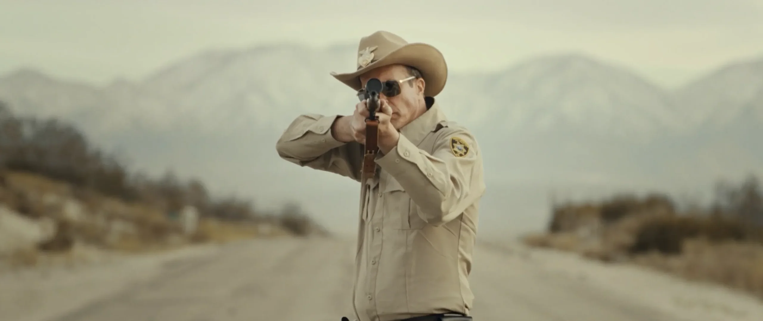 Sheriff Bilstein aiming a rifle on an isolated desert highway in Blood Star