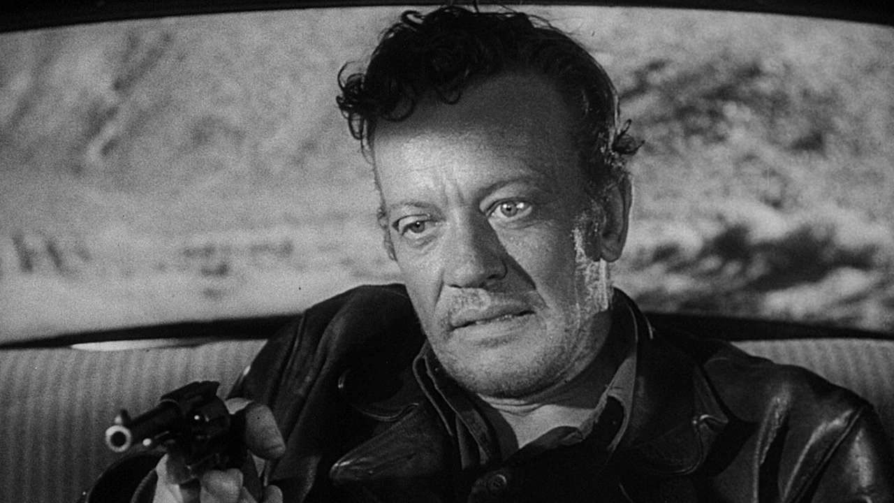 A black-and-white still of the fugitive gunman in the back seat of a car in The Hitch-Hiker (1953)