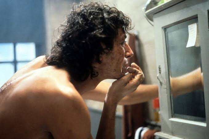 Seth Brundle examining himself in a bathroom mirror in The Fly