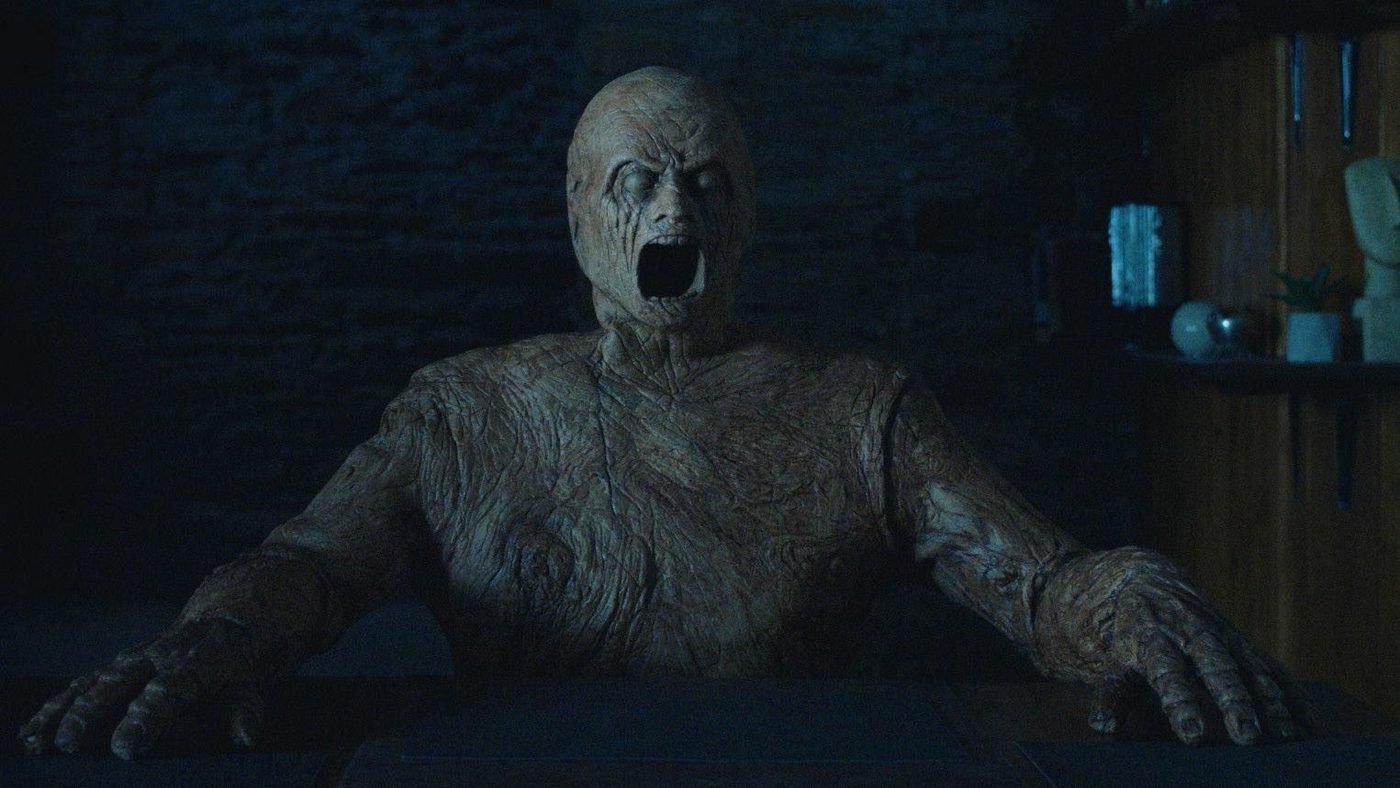 The screaming wooden mannequin figure emerging from behind a desk in Oddity (2024)