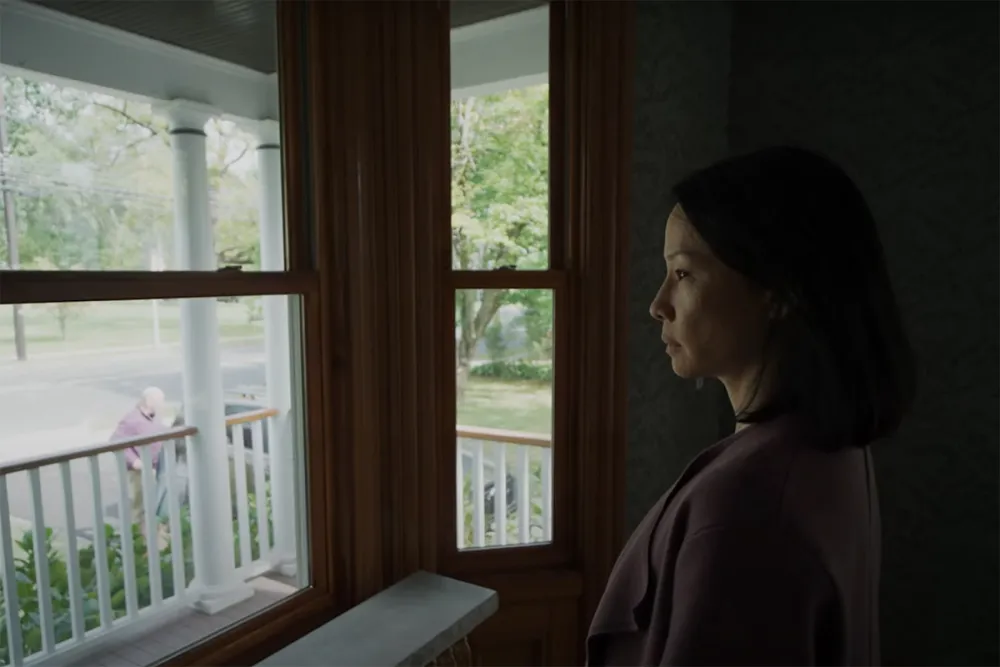 A woman looking out through a window with blurred lights visible outside in Presence (2024)