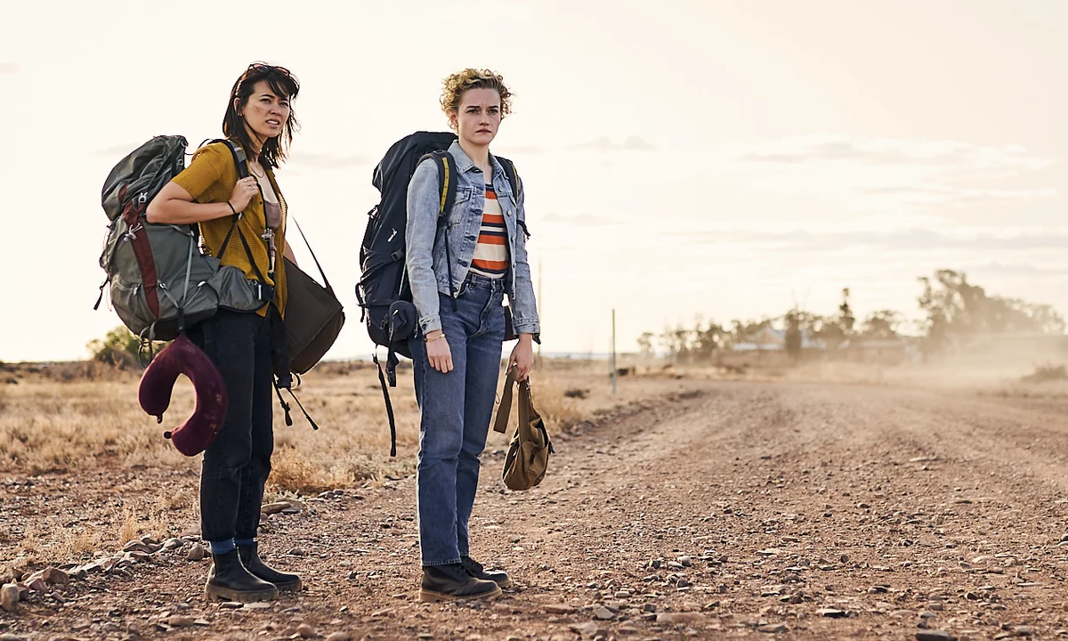 Two backpackers standing on a dusty outback road with their bags in The Royal Hotel (2023)