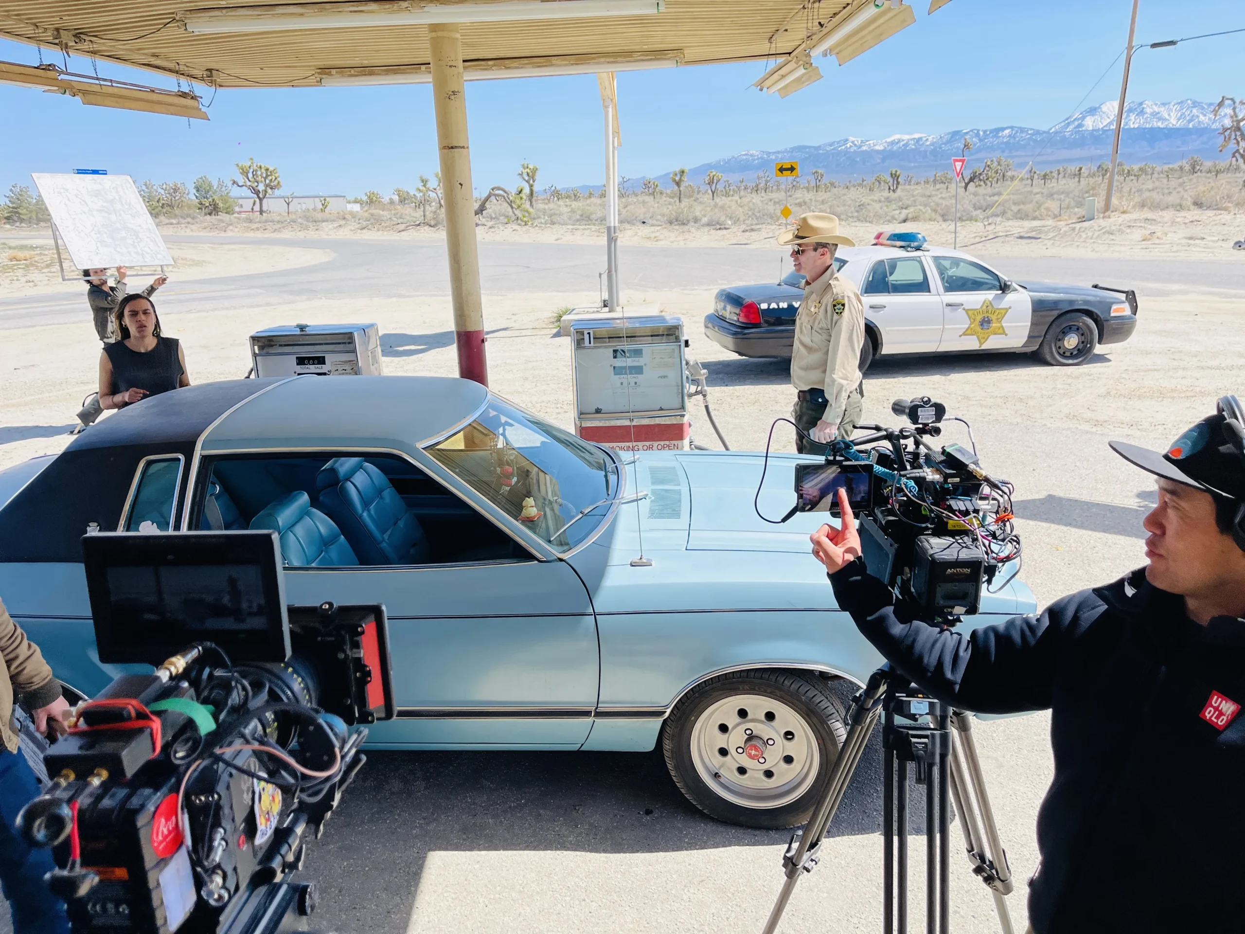 The sheriff's cruiser, camera crew and cast filming at a desert gas station for Blood Star