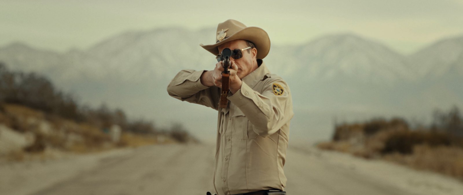 Sheriff Bilstein aiming a rifle down a desert highway in Blood Star